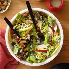 a salad with apples, lettuce and cheese in a white bowl on a wooden table