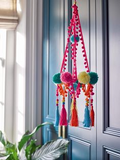 a colorful wind chime hanging from the side of a door with tassels and pom - poms