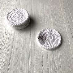 two white crocheted coasters sitting on top of a wooden table next to each other