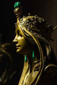 a gold statue with green jewels on it's head and wearing a tiara