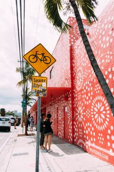 two people are standing on the sidewalk next to a building with a bicycle painted on it