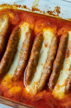 several sausages are in a casserole dish with sauce and cheese on top