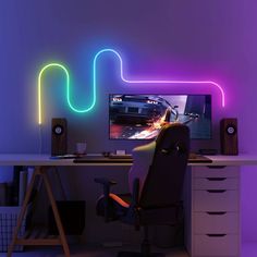 a computer desk with a monitor and speakers on it in front of a neon colored wall