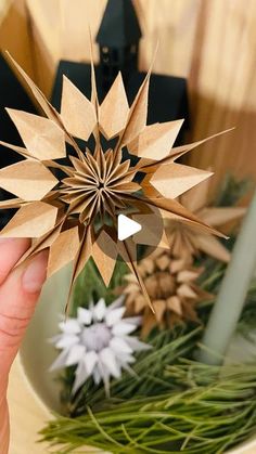 a person is holding up a paper star ornament in front of christmas decorations