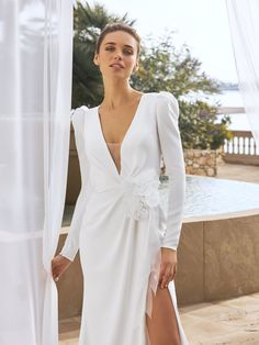 a woman standing next to a pool wearing a white dress