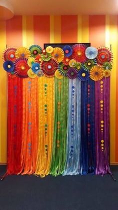 a rainbow colored backdrop with flowers and ribbons on the wall in front of it is an orange striped wall