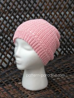 a white mannequin head wearing a pink knitted hat on top of a wicker table