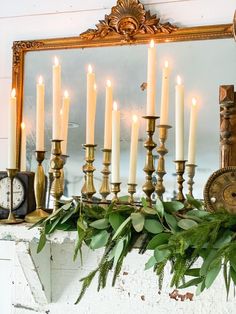 a mantel with candles and greenery in front of a mirror