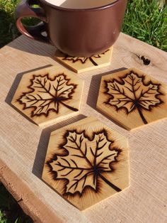 four maple leaf coasters sitting on top of a wooden table next to a cup