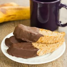 two pieces of bread on a plate with chocolate frosting next to a cup of coffee