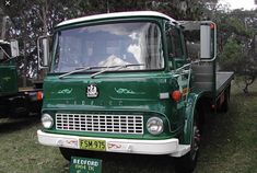 an old green truck is parked in the grass with other trucks behind it on display