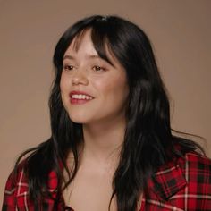 a woman with long black hair wearing a red and black plaid shirt smiles at the camera