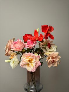 a vase filled with different colored flowers on top of a wooden table next to a gray wall