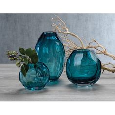 three blue vases sitting next to each other on top of a wooden table with branches in the background