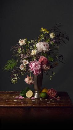 a vase filled with lots of flowers sitting on top of a wooden table next to lemons