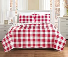 a red and white checkered comforter set on a bed in a room with windows