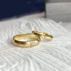 two gold wedding rings with diamonds on top of white furnishing, close up