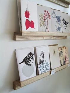 some cards are hanging on the wall with wooden shelves holding them and two small paintings