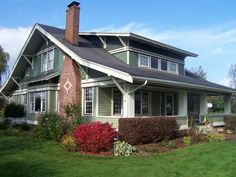 a green house with red flowers in the front yard and bushes on the other side