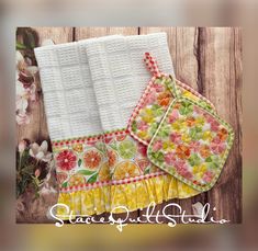 two kitchen towels are sitting next to each other on a wooden surface with flowers in the background