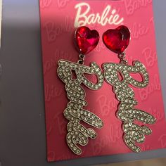 Elevate Your Fashion Game With These Stunning Barbie Doll Movie Fashionista Pink Silver Rhinestone Logo Statement Earrings. These Dangle/Drop Earrings Are Perfect For Any Occasion And Add A Touch Of Feminine Elegance To Your Ensemble. The Earrings Are Made Of High-Quality Rhinestone And Silver Metal, Ensuring Long-Lasting Durability. The Beautiful Pink Color Of The Main Stone Complements The Silver Metal And Adds A Pop Of Color To Your Outfit. The Earrings Are A Great Gift For Any Barbie Fan Or Barbie Jewelry, Pink Heart Earrings, Feminine Elegance, Pom Pom Earrings, Trending Bracelets, Gem Earrings, Barbie Fashionista, Barbie Accessories, Silver Logo