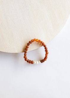 a beaded bracelet with an orange and white bea sits on top of a piece of wood