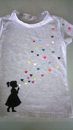 a child's t - shirt with hearts flying in the air and a silhouette of a girl holding a heart shaped balloon