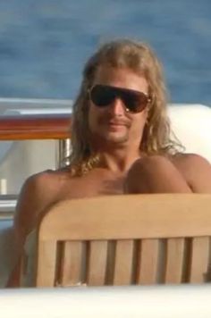 a shirtless man sitting in the back of a boat with sunglasses on his head