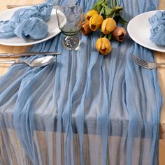 the table is set with plates, silverware and tulips in blue cloth