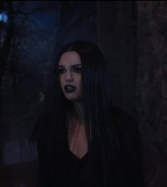 a woman with long black hair standing in the dark