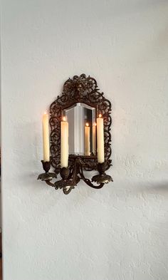 three candles are lit in front of an ornate mirror on the wall above a sink