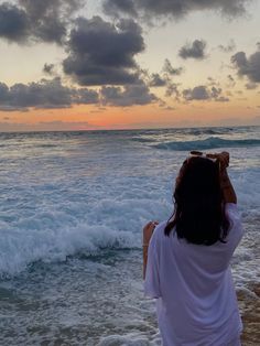 a woman standing on top of a sandy beach next to the ocean under a cloudy sky