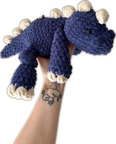 a hand holding up a crocheted blue and white stuffed animal that looks like a dinosaur