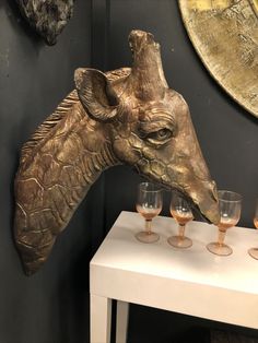 a giraffe head with four wine glasses on a small table in front of it