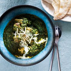 a blue bowl filled with spinach and cheese on top of a table next to bread