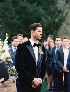 a man in a tuxedo standing next to a barrel with flowers on it