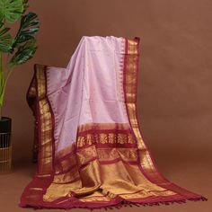 Soft as a gentle flush, the blush pink Gadwal silk saree glows with warmth, all-over woven red checks shimmering like tender rose petals. Gold zari woven red temple border and pallu gleam like sacred flames, while the embroidered red blouse adds a touch of passionate elegance. Together, they create a tapestry of loving devotion, a celebration of the heart's deepest emotions. She who wears this saree is a goddess of love, her beauty and grace as radiant as a rose in bloom, her spirit as fierce as a burning flame * Gadwal silk saree for special occasions. * Crafted from the premium quality fabric. * Supplied with a readymade blouse. * The blouse comes with an added allowance, and it can be altered to a standard size of 34"-42" on request. * Dry clean only to maintain colour and quality.  Not Pink Cotton Silk Traditional Wear For Transitional Season, Transitional Pink Cotton Silk Traditional Wear, Pink Paithani Silk Pre-draped Saree For Traditional Ceremonies, Pink Paithani Silk Pre-draped Saree For Eid, Pink Paithani Silk Pre-draped Saree, Pink Pre-draped Cotton Silk Saree With Zari Weaving, Pink Cotton Silk Traditional Dupatta, Pink Cotton Silk Traditional Wear For Festivals, Traditional Pink Cotton Silk Dupatta