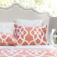 a bed with orange and white pillows on it's headboard in front of a window