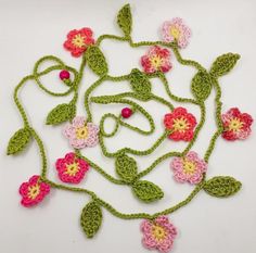 crocheted flowers and leaves are arranged on a white surface with red, yellow, pink, and green stems