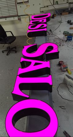 the neon pink sign is next to an office chair and computer desk in the background