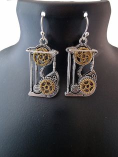 Hand made in the UK, steam punk clock face earrings.  each earring comprises A Carriage clock skeleton with individually positioned gold plated cogs to the top and bottom. An added raised silver top bar completes the look.  the earring hooks are hand formed french style hypo-allergenic. Materials used: Silver plated Tibetan steel Brass gold plated Tibetan steel Hypoallergenic steel 0.8mm silver plated wire Gold Steampunk Earrings, Steampunk Metal Earrings For Pierced Ears, Steampunk Gold Dangle Jewelry, Gold Steampunk Dangle Jewelry, Steampunk Silver Dangle Jewelry, Handmade Steampunk Gold Earrings, Silver Steampunk Dangle Jewelry, Handmade Silver Steampunk Earrings, Handmade Gold Steampunk Earrings