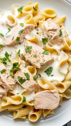 a white plate topped with pasta and meat covered in sauce, garnished with parsley