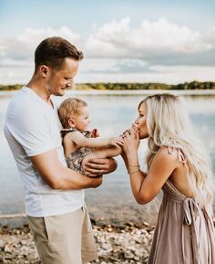 a man holding a baby while standing next to a woman with her hands around him