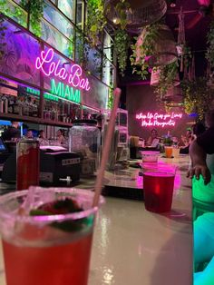 a person sitting at a bar with drinks in front of them and neon signs above the bar