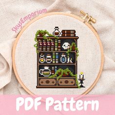 a cross stitch bookcase with plants and books on it is shown in the hoop