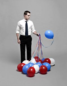 a man standing in front of balloons that are red, white and blue with a black tie