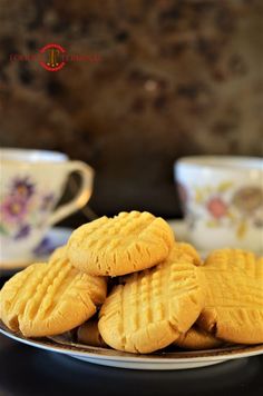 some cookies are stacked on a plate with tea cups in the backgroung