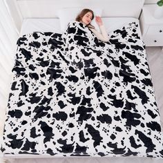 a woman laying in bed under a black and white cow print blanket on the floor