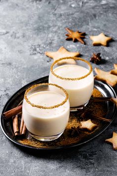 two glasses filled with white liquid on top of a plate next to cinnamon sticks and star shaped cookies