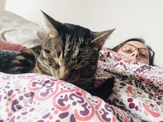 a woman laying in bed next to a cat with her head on the pillow and eyes closed